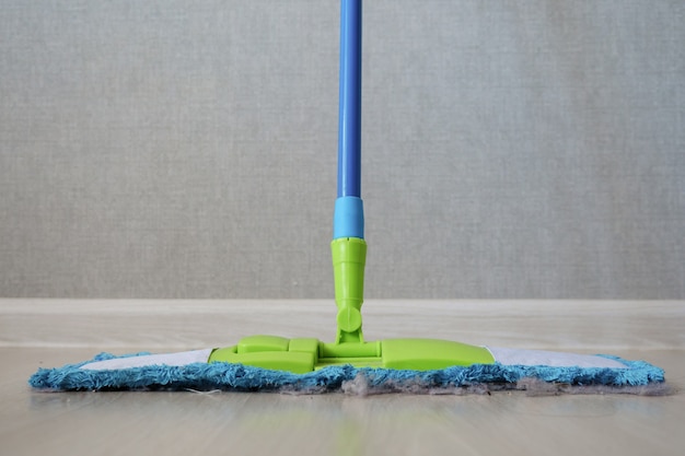 Trapeador de limpieza con polvo en el piso de madera del dormitorio, vista frontal