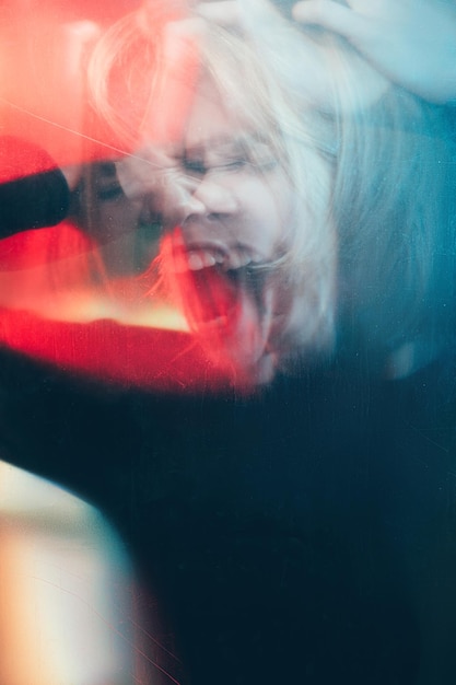 Trastorno mental Ataque de pánico Silueta desenfocada de mujer psicópata cabreada con dolor de cabeza gritando en luz roja azul bokeh con vieja película polvo arañazos manchas efecto doble exposición