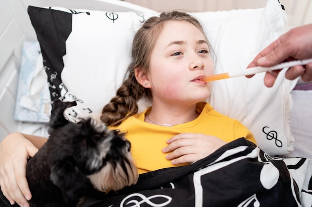 Tratamento da criança que ela está bebendo xarope medicinal menina doente está deitada na cama com seu cachorrinho