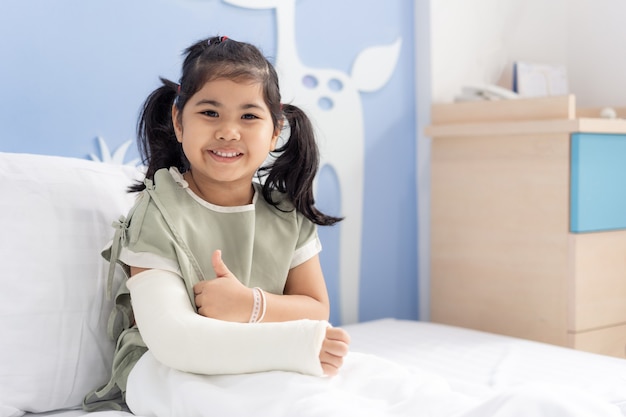 Foto tratamento de menina asiática no hospital, deitada na cama, machucando com o braço quebrado nas costas da cirurgia.