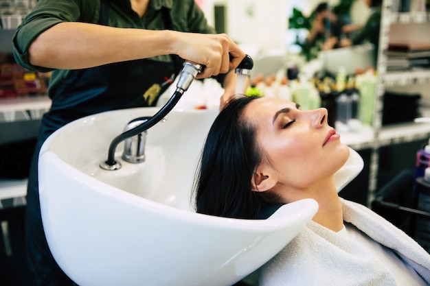 Tratamento de spa. Vista superior das mãos do cabeleireiro lavando o cabelo de sua cliente no salão antes do processo de penteado.