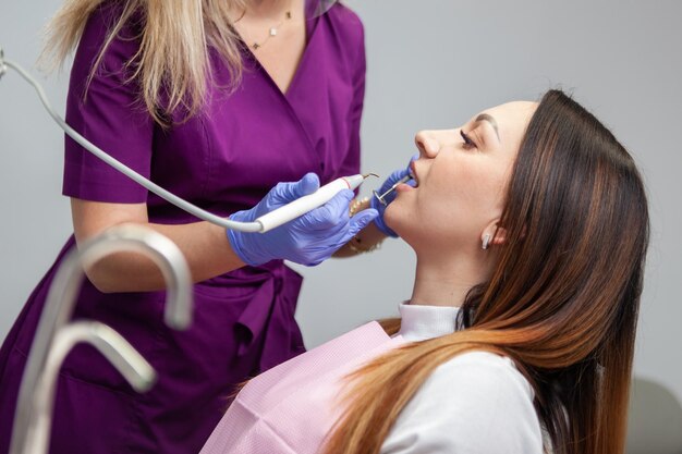Tratamento dentário Dentistas usando broca dentária e espelho ao examinar a boca da mulher na clínica Tratamento profissional na clínica dentária