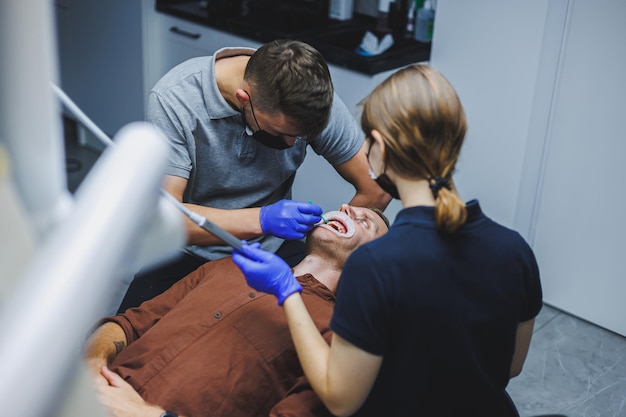 Tratamento dentário dos dentes Um jovem na consulta do dentista Um médico e um assistente tratam os dentes de um paciente em um consultório odontológico