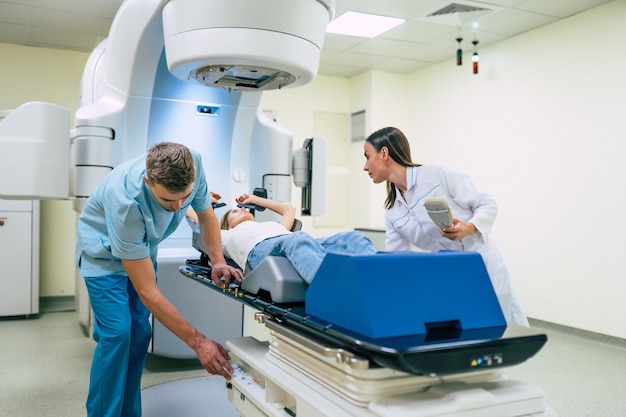 Tratamento do câncer em uma clínica médica privada moderna ou hospital com um acelerador linear. Equipe de médicos profissionais trabalhando enquanto a mulher está se submetendo à radioterapia para câncer
