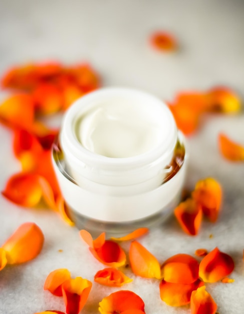 Tratamento facial anti-envelhecimento cuidado da pele e conceito de spa - Creme hidratante para rosto de beleza e pétalas de flores em mármore produto cosmético de luxo