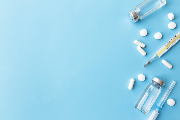Tratamento medicamentoso, conceito de vacinação. Termômetro, frascos de vacina, injeção, seringa, pílulas sobre fundo azul.