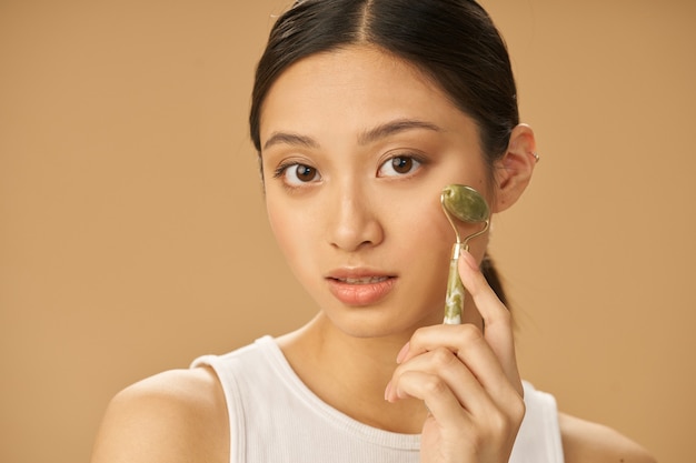 Tratamiento de belleza facial hermosa mujer joven mirando a la cámara mientras recibe masaje facial usando