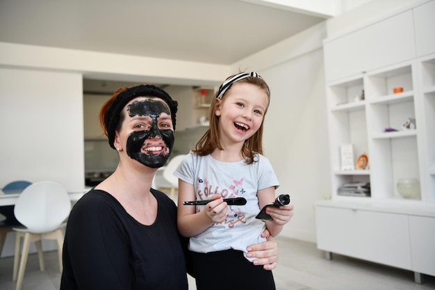 Tratamiento de belleza familiar en el hogar durante la pandemia del coronavirus permanecer en cuarentena en el hogar. Madre e hija pequeña hacen una máscara facial.