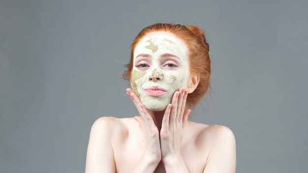 Tratamiento de belleza. La niña aplicando una mascarilla de arcilla verde para la cara. procedimiento estético