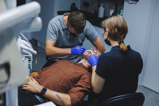 Tratamiento dental de los dientes Un joven en una cita con el dentista Un médico y un asistente tratan los dientes de un paciente en un consultorio dental