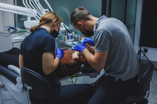 Tratamiento dental de los dientes Un joven en una cita con el dentista Un médico y un asistente tratan los dientes de un paciente en un consultorio dental