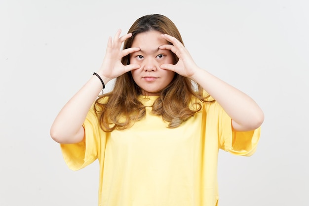 Tratando de abrir los ojos con los dedos de una hermosa mujer asiática con camiseta amarilla aislada en blanco