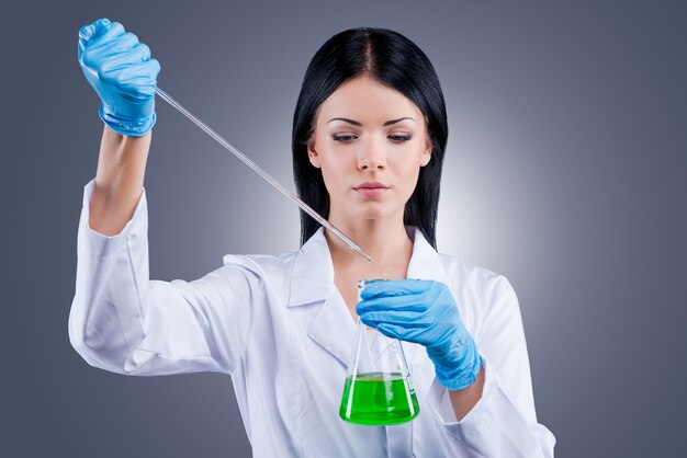 Tratando de curar el mundo. Hermosa doctora en uniforme blanco sosteniendo frascos mientras está de pie contra el fondo gris