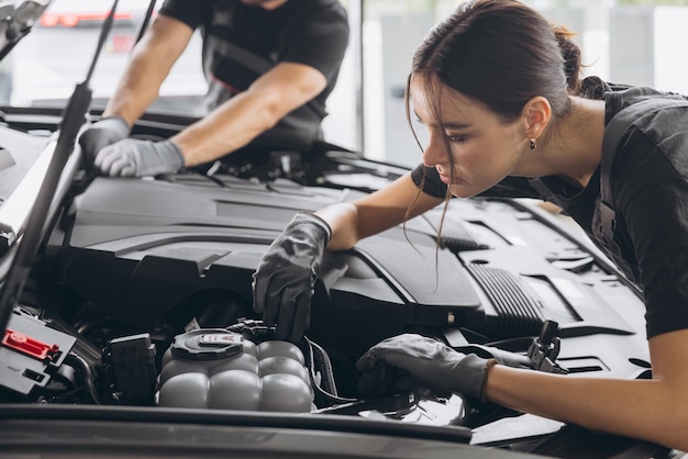 Tratando de identificar la fuente del problema Primer plano de dos mecánicos hombre y mujer trabajando juntos en el capó abierto en un coche en un taller de reparación de automóviles