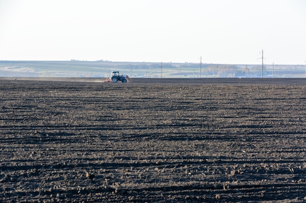 Trator agrícola com arado em um campo em uma fazenda no dia ensolarado. Fazendeiro em trator preparando a terra. É a época de arar. Copie o espaço.