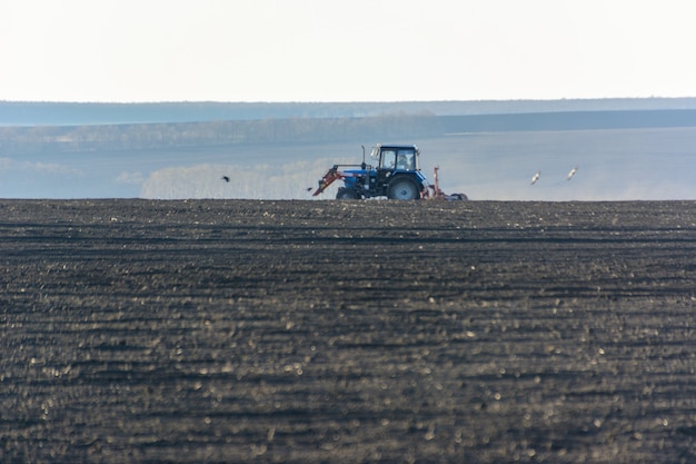 Trator agrícola com arado em um campo em uma fazenda no dia ensolarado. Fazendeiro em trator preparando a terra. É a época de arar. Copie o espaço.