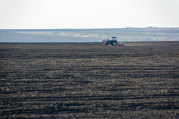 Trator agrícola com arado em um campo em uma fazenda no dia ensolarado. Fazendeiro em trator preparando a terra. É a época de arar. Copie o espaço.