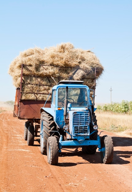 Trator com carroça de feno em estrada rural