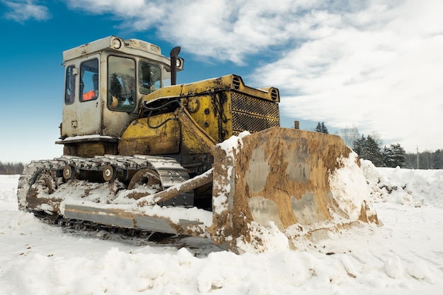 Trator de esteira amarela com um balde funciona no inverno, limpando a estrada da neve.