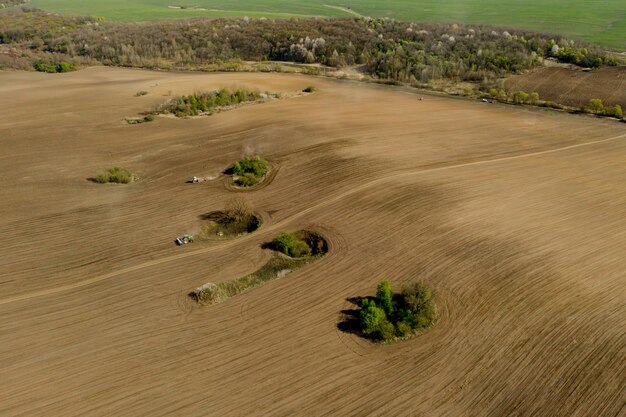 Trator grande de vista aérea cultivando um campo seco Trator de vista aérea de cima para baixo cultivando solo e semeando um campo seco Trator aéreo corta sulcos no campo agrícola para semear