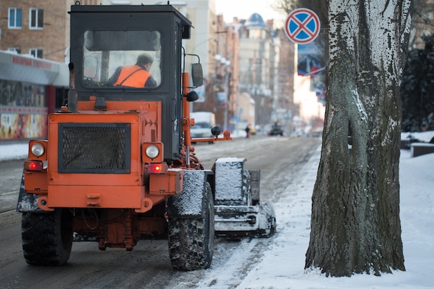 Trator limpando a estrada da neve. A escavadeira limpa as ruas de grandes quantidades de neve na cidade. Trabalhadores varrem neve da estrada no inverno, limpando a estrada da tempestade de neve.