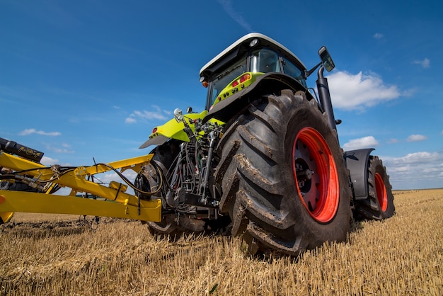 Trator verde em um campo com equipamento de restolho, vista inferior