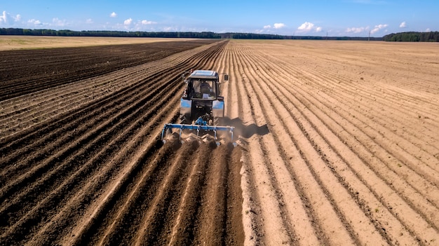 Trator - vista aérea de um trator no trabalho - cultivando um campo na primavera com céu azul - máquinas agrícolas