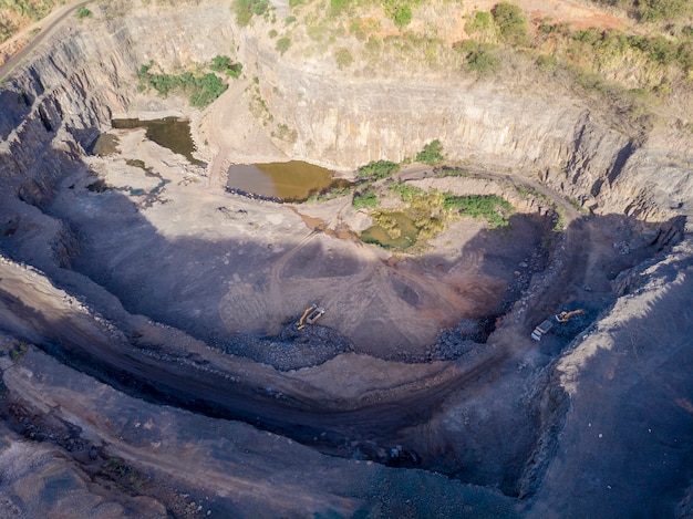 Tratores e caminhões removendo pedras de dentro de um buraco de pedreira