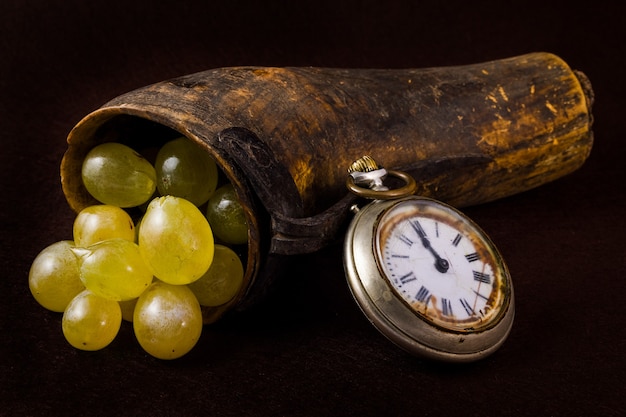 Trauben in einem alten Horn und einer antiken Uhr.