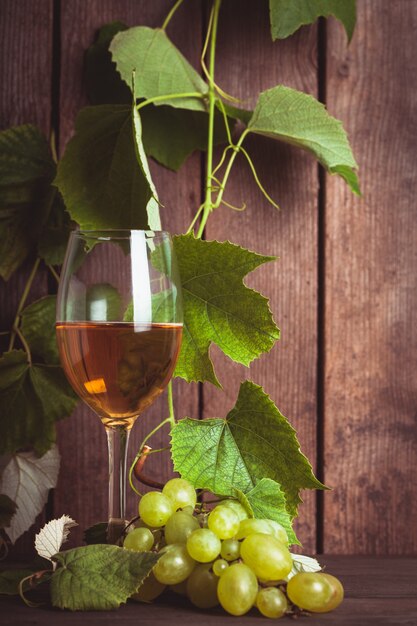 Trauben mit Blättern und Glas Wein auf dem Holzhintergrund