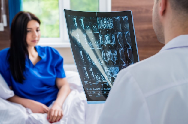 Foto traumatólogo mostrando una película de resonancia magnética al paciente en el hospital.