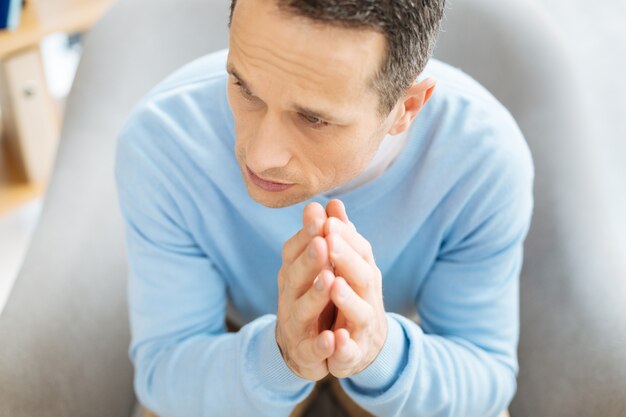 Foto traurig sein. draufsicht eines freudlosen unglücklichen launischen mannes, der seine hand zusammenhält, während er von den depressiven gedanken traurig ist