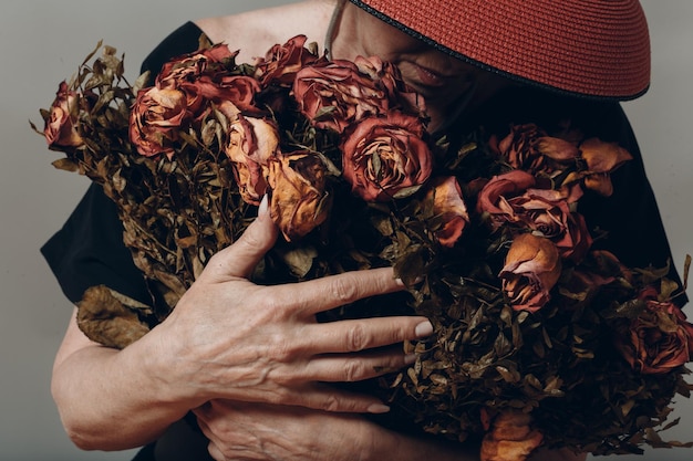 Traurige ältere Frau berührt Strauß verwelkter Rosen