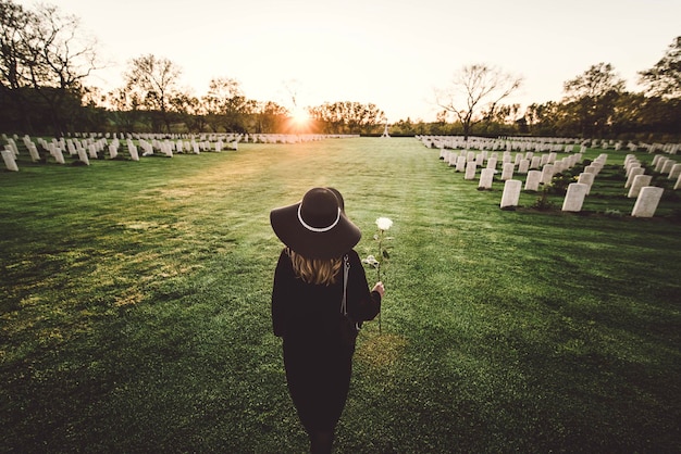 Traurige Frau auf dem Friedhof mit Rosenstrauß in der Hand