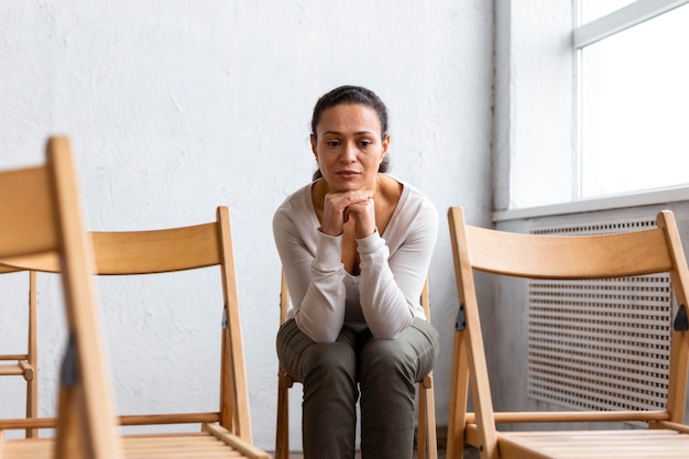 Foto traurige frau, die auf einem stuhl bei einer gruppentherapiesitzung sitzt