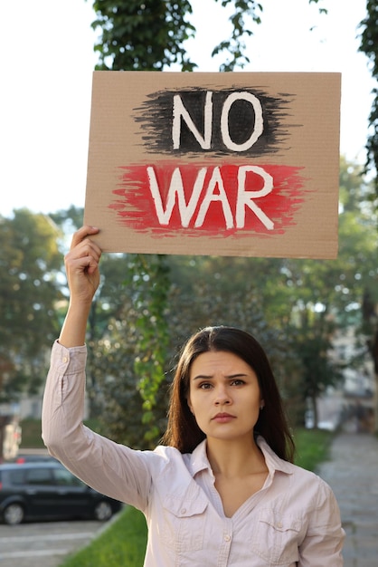 Traurige Frau, die ein Plakat mit den Worten No War auf der Straße der Stadt hält