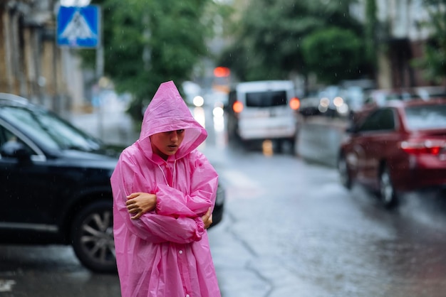 Traurige Frau in einem Regenmantel auf der Straße im Regen