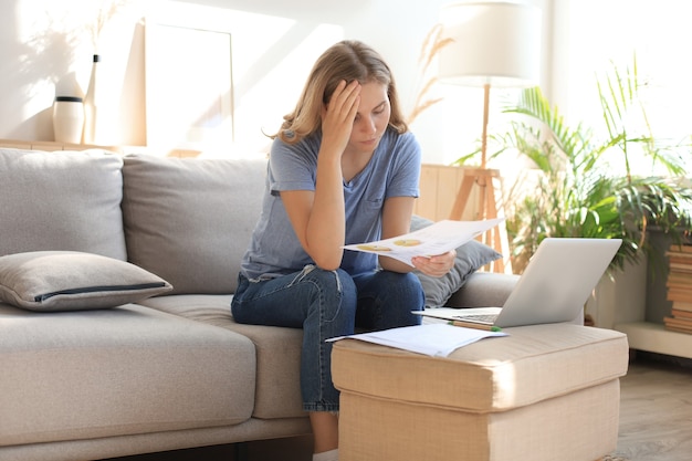 Traurige Frau mit den Rechnungen, die auf einem Sofa im Wohnzimmer sitzen