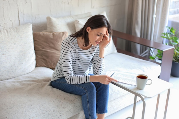 Traurige Frau mit den Rechnungen, die auf einem Sofa im Wohnzimmer sitzt