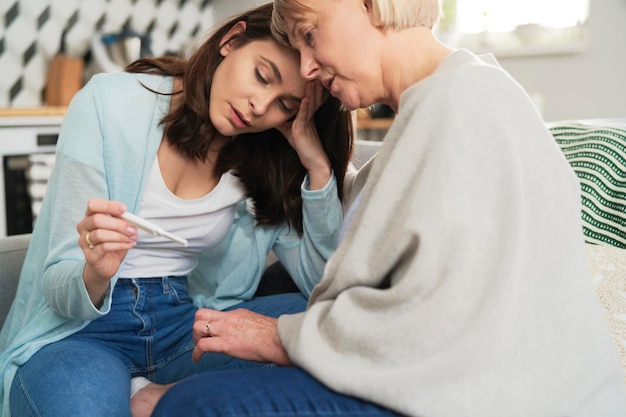 Traurige Frau mit negativem Schwangerschaftstest mit ihrer Mutter