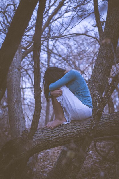 Traurige Frau sitzt auf einem Zweig im Wald
