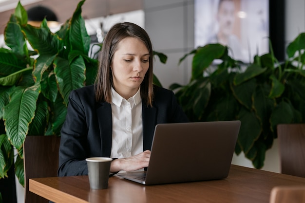 Traurige Geschäftsfrau mit dunklen kurzen Haaren, die am Computer arbeitet und gelangweilt ist