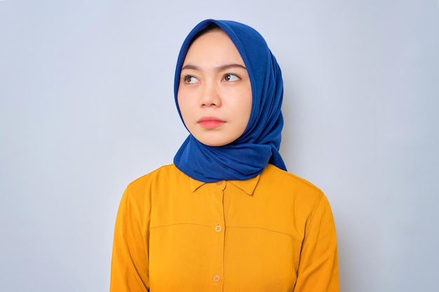 Traurige junge asiatische muslimische Frau in orangefarbenem Hemd, die mit unzufriedenem Traurigkeitsgesicht isoliert über weißem Hintergrund wegschaut