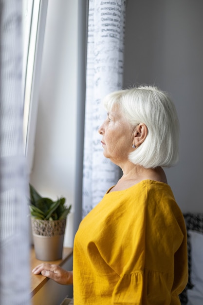 Traurige kaukasische Frau Jahre alt schaut aus dem Fenster Hoffnung Konzept Konzept Heimquarantäneprävention ...