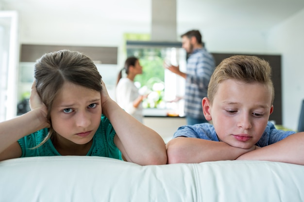 Traurige kinder, die sich auf sofa stützen, während eltern streiten