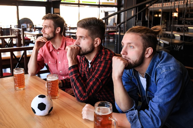 Traurige männliche Fußballfans, die das Spiel an der Bar beobachten und Bier trinken.
