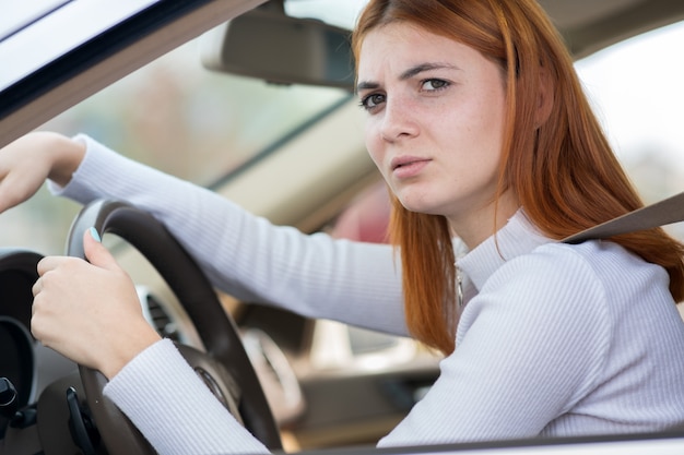 Traurige müde junge Fahrerin, die hinter dem Autolenkrad sitzt