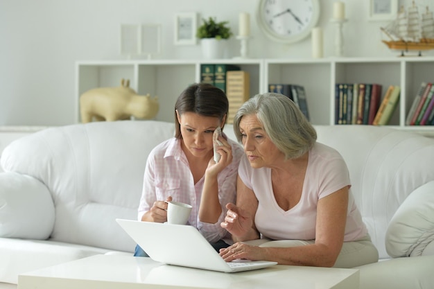 Traurige Mutter und Tochter sitzen zu Hause mit Laptop am Tisch