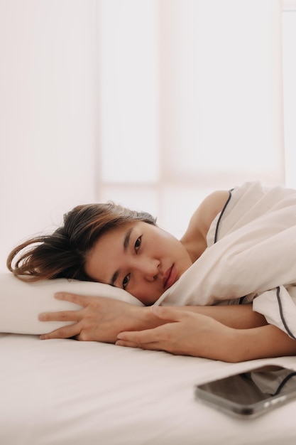 Traurige und deprimierte asiatische Frau, die morgens wach liegt, um schwach aus dem Bett aufzustehen