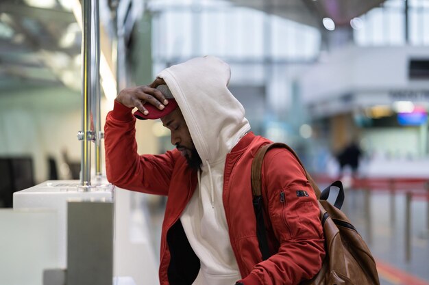 Foto trauriger afrikaner, der in der nähe des check-in-schalters steht und sich wegen der flugstornierung frustriert fühlt
